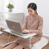 A woman is using a portable adjustable laptop desk stand to position a silver laptop on a wooden surface.