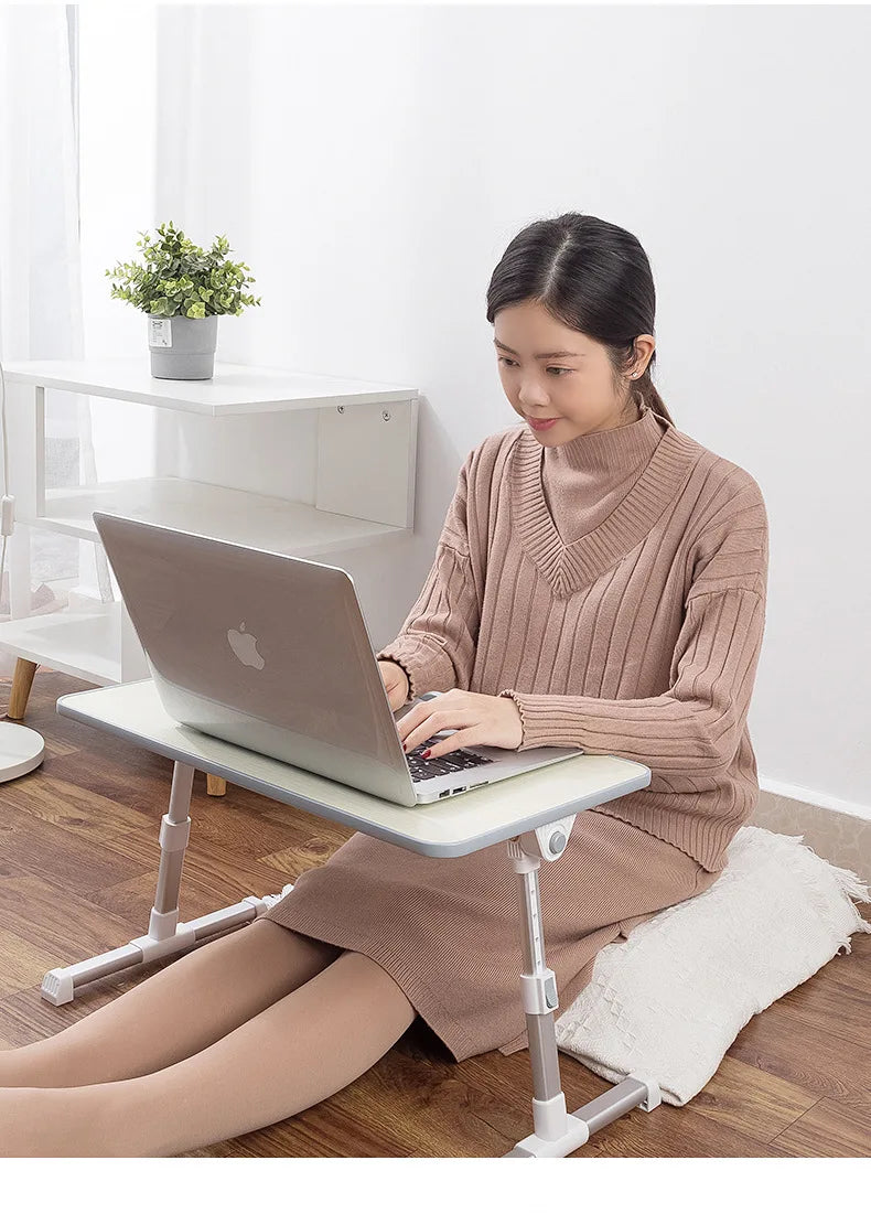 A woman is using a portable adjustable laptop desk stand to position a silver laptop on a wooden surface.