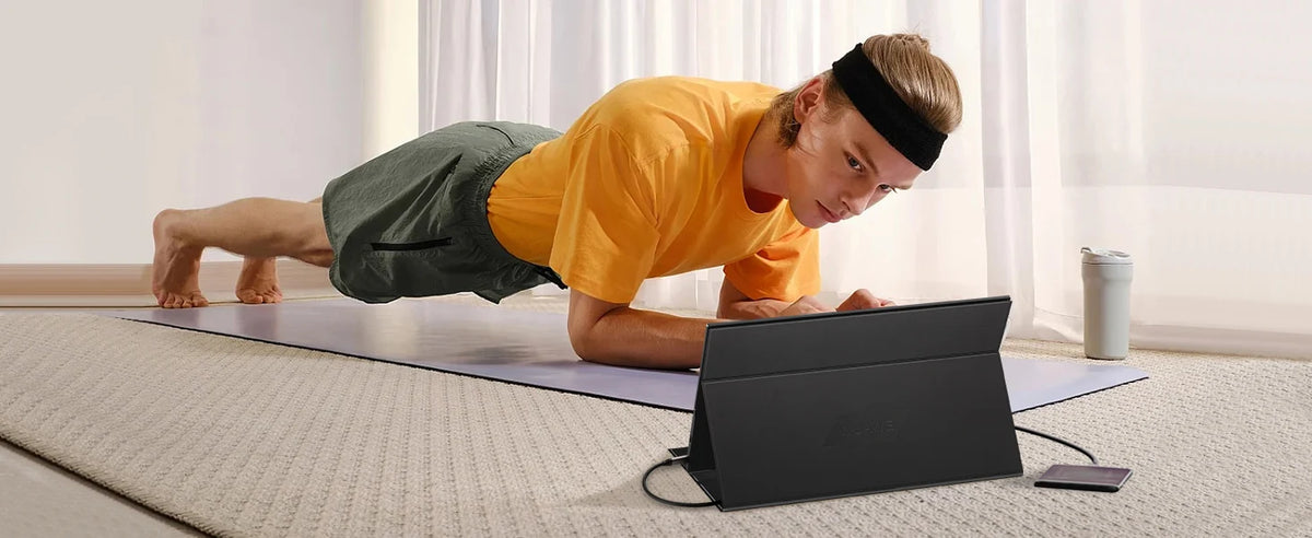 A person is using a portable laptop monitor while doing an exercise on a yoga mat.