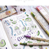 A set of three twin markers in various shades and colors laid out on a sheet of paper with watercolor illustrations.