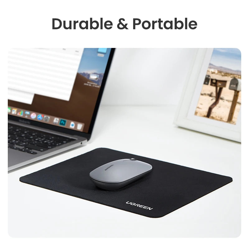 A black ergonomic mouse pad is shown on a white desk next to a laptop and a framed photo.