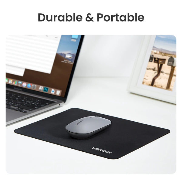 A black ergonomic mouse pad is shown on a white desk next to a laptop and a framed photo.