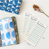 A set of twelve budget planner cards in six colors with a cash envelope design and a leather-bound notebook.