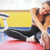 A woman is using a red yoga mat and a portable laptop monitor in a brightly lit gym setting.