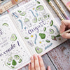 A hand writes 'FRESH AUGUST' in watercolor style on a notebook next to a set of three retro twin markers.