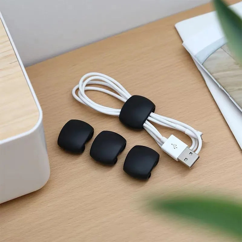 Black silicone cable organizer clips and a white USB connector lying on a wooden surface.