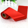 A roll of bright red satin ribbon lying on a white surface next to a white planter.