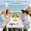 Five travel lights and a power bank are shown on a table outdoors with people enjoying a meal by the sea.