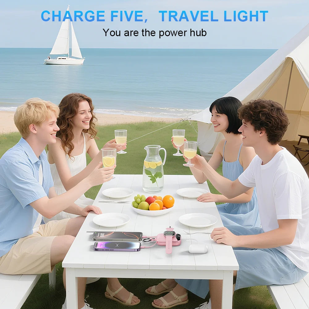 Five travel lights and a power bank are shown on a table outdoors with people enjoying a meal by the sea.