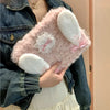 A pink fluffy rabbit plush case with white ears and a pink bow is being held by a person wearing a denim jacket.