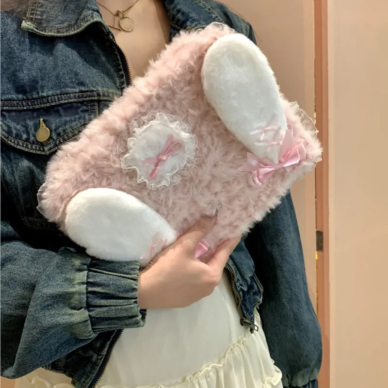 A pink fluffy rabbit plush case with white ears and a pink bow is being held by a person wearing a denim jacket.