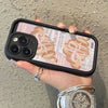 A hand holds an iPhone in a black case featuring a croissant newspaper pattern.