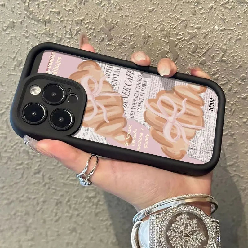 A hand holds an iPhone in a black case featuring a croissant newspaper pattern.