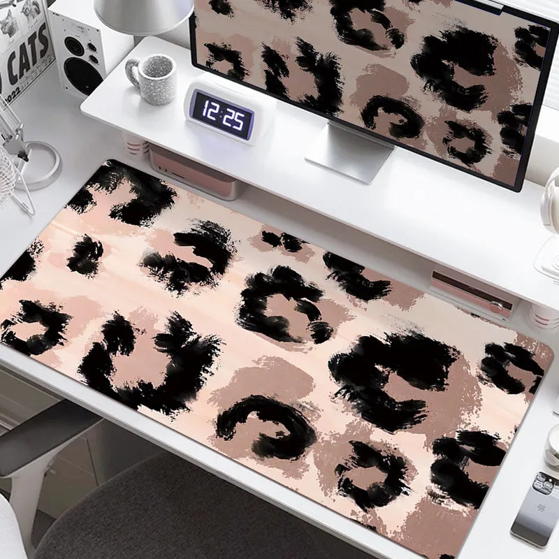 A large leopard print desk pad is displayed on a white desk next to a digital clock and a computer monitor.