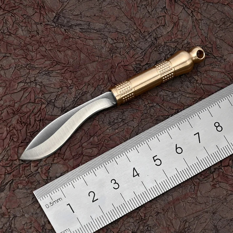 A polished brass fixed blade knife is shown next to a ruler, highlighting its size and craftsmanship.