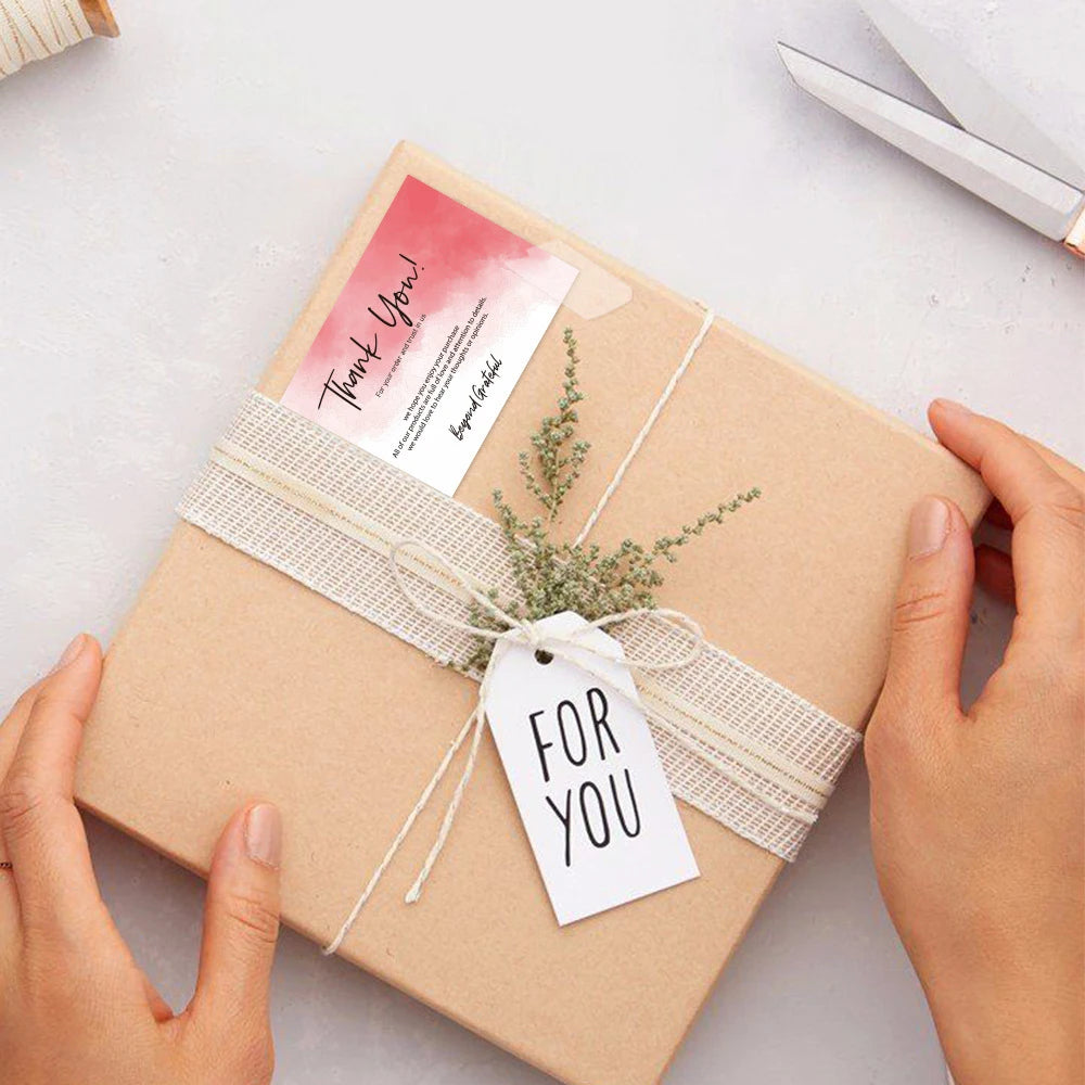 Hands are tying a natural twine bow on a kraft paper gift box with a thank you tag.