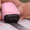 A hand holds a pink roller stamp with a black handle, positioned over a document.