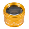 A round, gold-colored magnifying loupe with a glass lens and text indicating it is made in Germany.