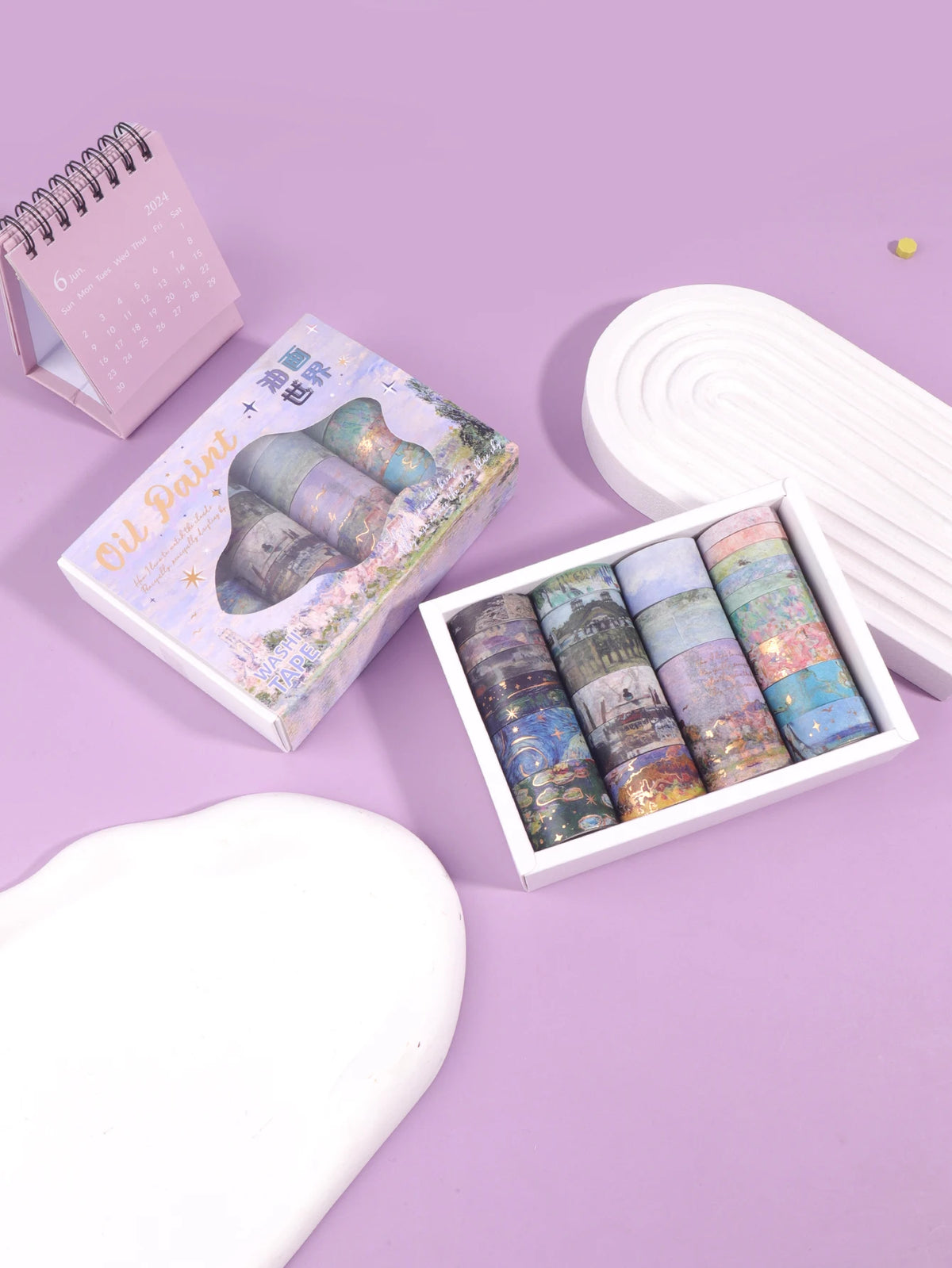A set of oil painting themed decorative washi tape rolls displayed next to a sketchbook and on a purple background.