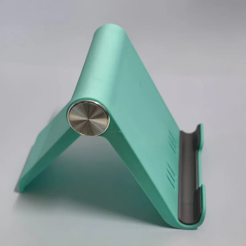 A teal foldable desktop phone holder shown from the side, featuring a metal hinge and a slot for a phone.
