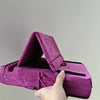 A hand holds a purple velvet foldable tablet pillow stand with a pocket open.