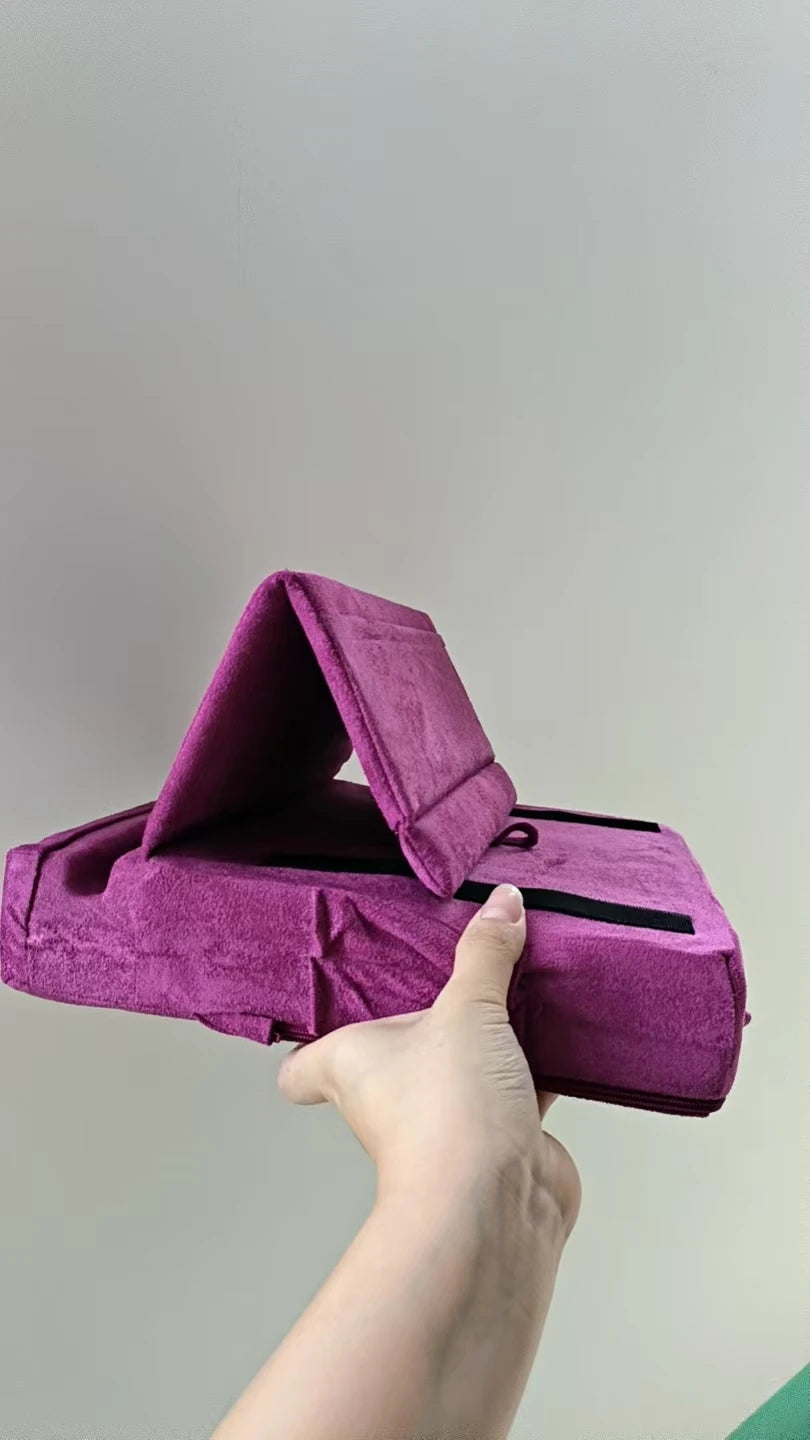 A hand holds a purple velvet foldable tablet pillow stand with a pocket open.