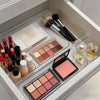 A clear acrylic drawer organizer set containing various makeup brushes and cosmetic products in a white box.