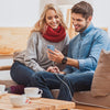 A smiling couple is using a USB-C fast charge cable to charge an iPhone while sitting on a couch.