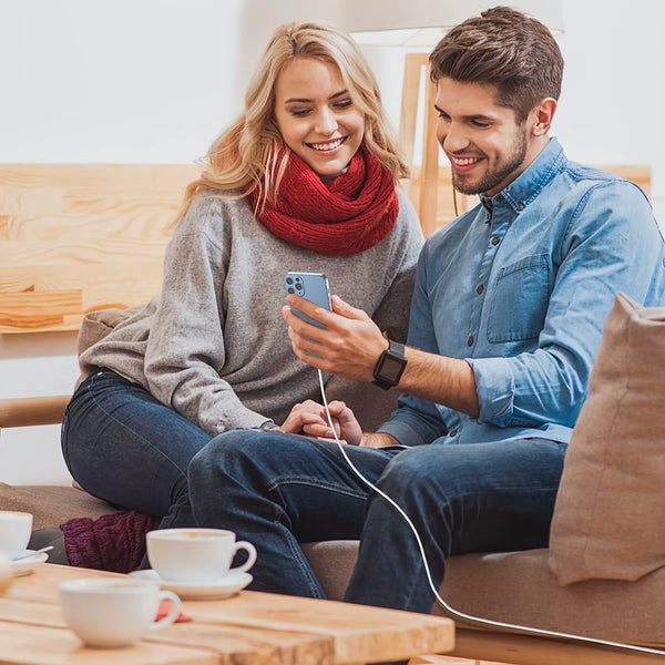A smiling couple is using a USB-C fast charge cable to charge an iPhone while sitting on a couch.
