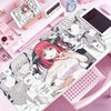 A pink mouse pad featuring anime characters and illustrations is displayed on a desk.