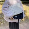 A person is holding a light pink padded laptop sleeve case with a quilted pattern outdoors.