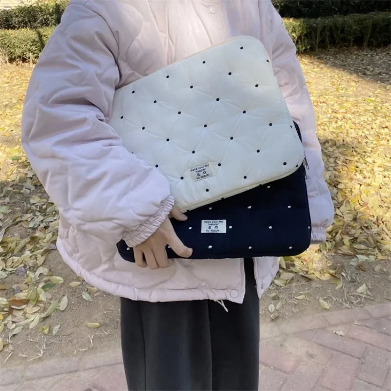 A person is holding a light pink padded laptop sleeve case with a quilted pattern outdoors.
