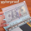 A clear waterproof envelope with a zipper holds a $100 bill and is shown next to a notebook.