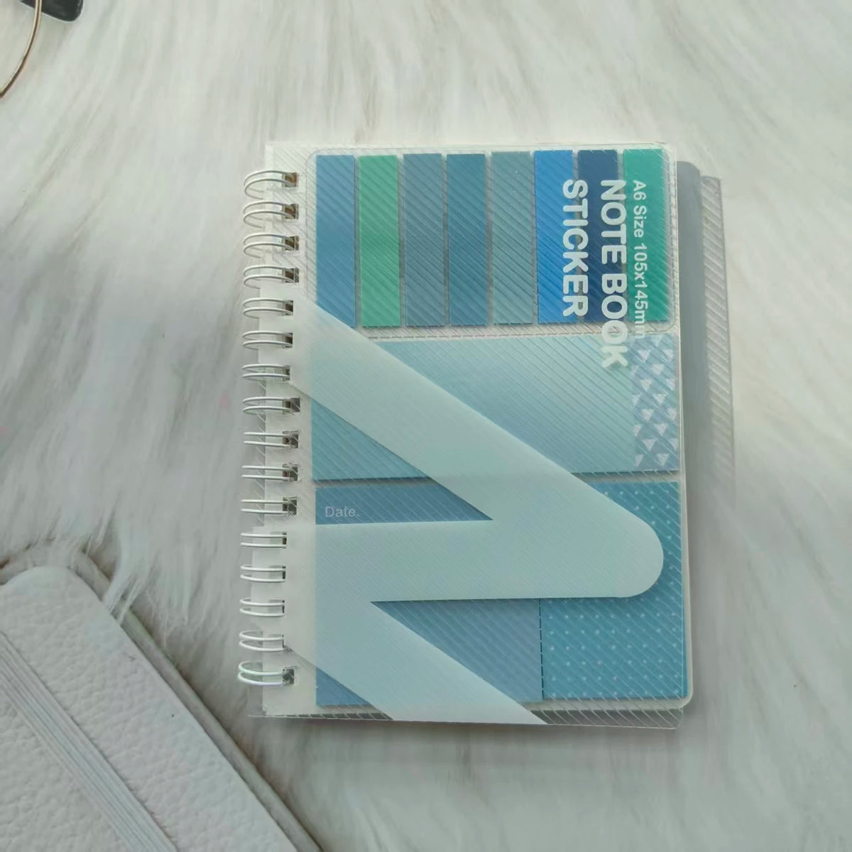 A stack of A6 size sticky note notebook with a loop closure featuring various shades of blue and teal.