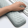 A hand rests on a gray ergonomic keyboard wrist rest pad, demonstrating massage patterns for comfortable typing.