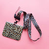 A leopard print ID holder with a black leather lanyard and keychain against a pink background.