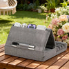 A gray foldable tablet pillow stand with a pocket holding several electronic devices rests on a wooden table outdoors.