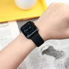 A close-up of a black Apple Watch on a wrist, next to a yellow surface and some printed paper.