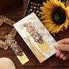 A hand holds a vintage artistic metal bookmark with a floral design and gold tassel against a dark wooden background.