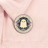A round enamel pin featuring a white ghost with butterfly wings and text that reads Living the dream! One nightmare at a time