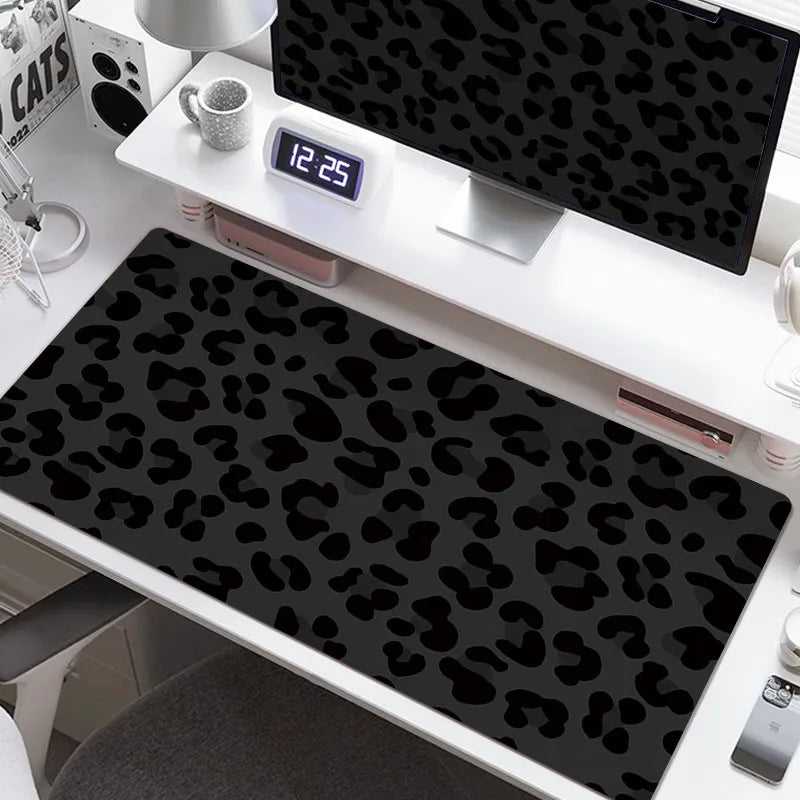 A black leopard print desk pad is displayed on a white desk next to a digital clock and a laptop.