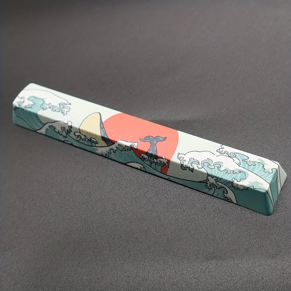 Rechteckiges Keycap-Set mit Motiv von Bergen, Wellen und einer roten Sonne auf blauem Hintergrund.