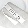 A white stainless steel bookmark with a tassel resting on a gray fabric surface.