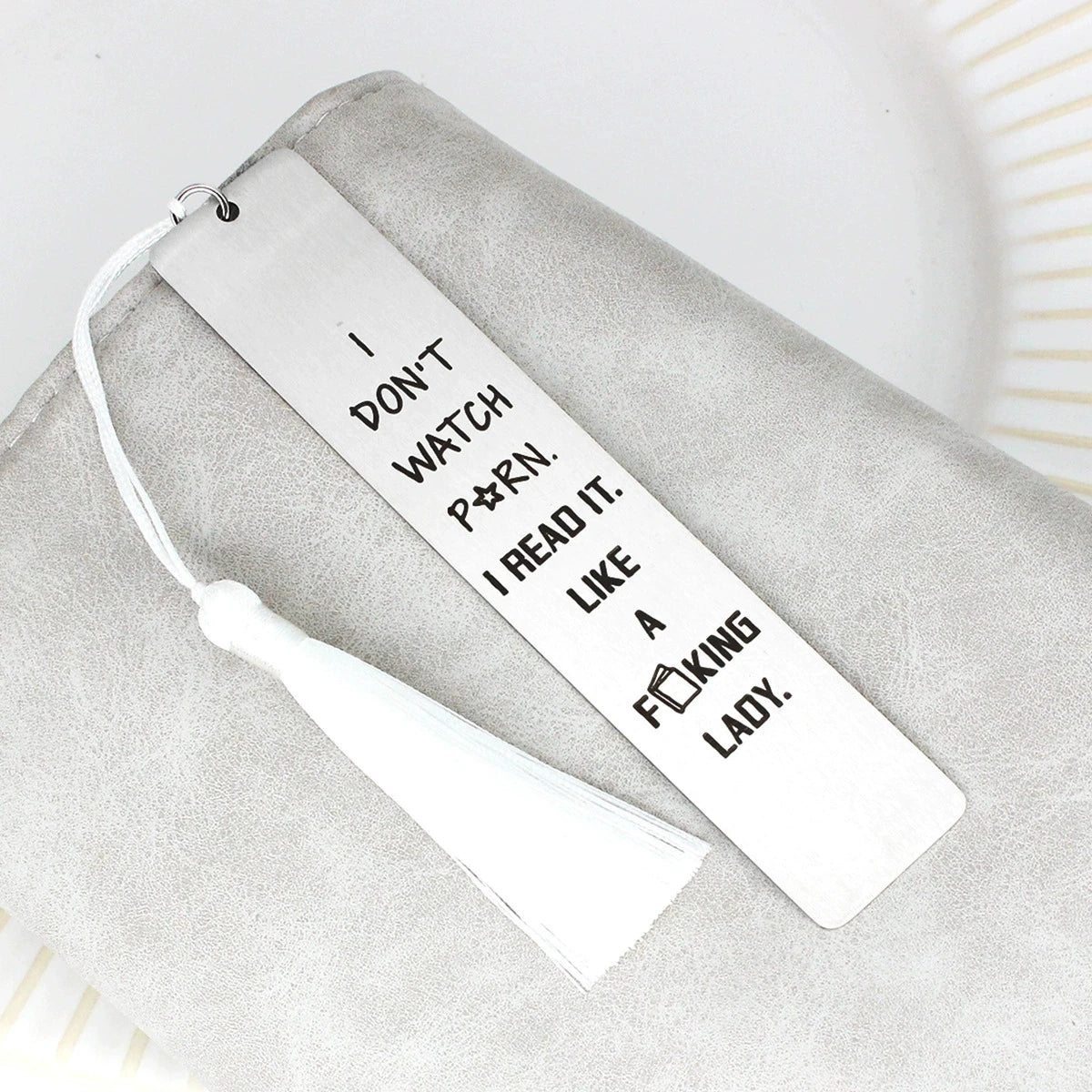 A white stainless steel bookmark with a tassel resting on a gray fabric surface.