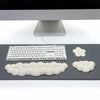 Un set de trois repose-poignets en forme de nuage blanc et un clavier argenté sur une surface gris foncé.