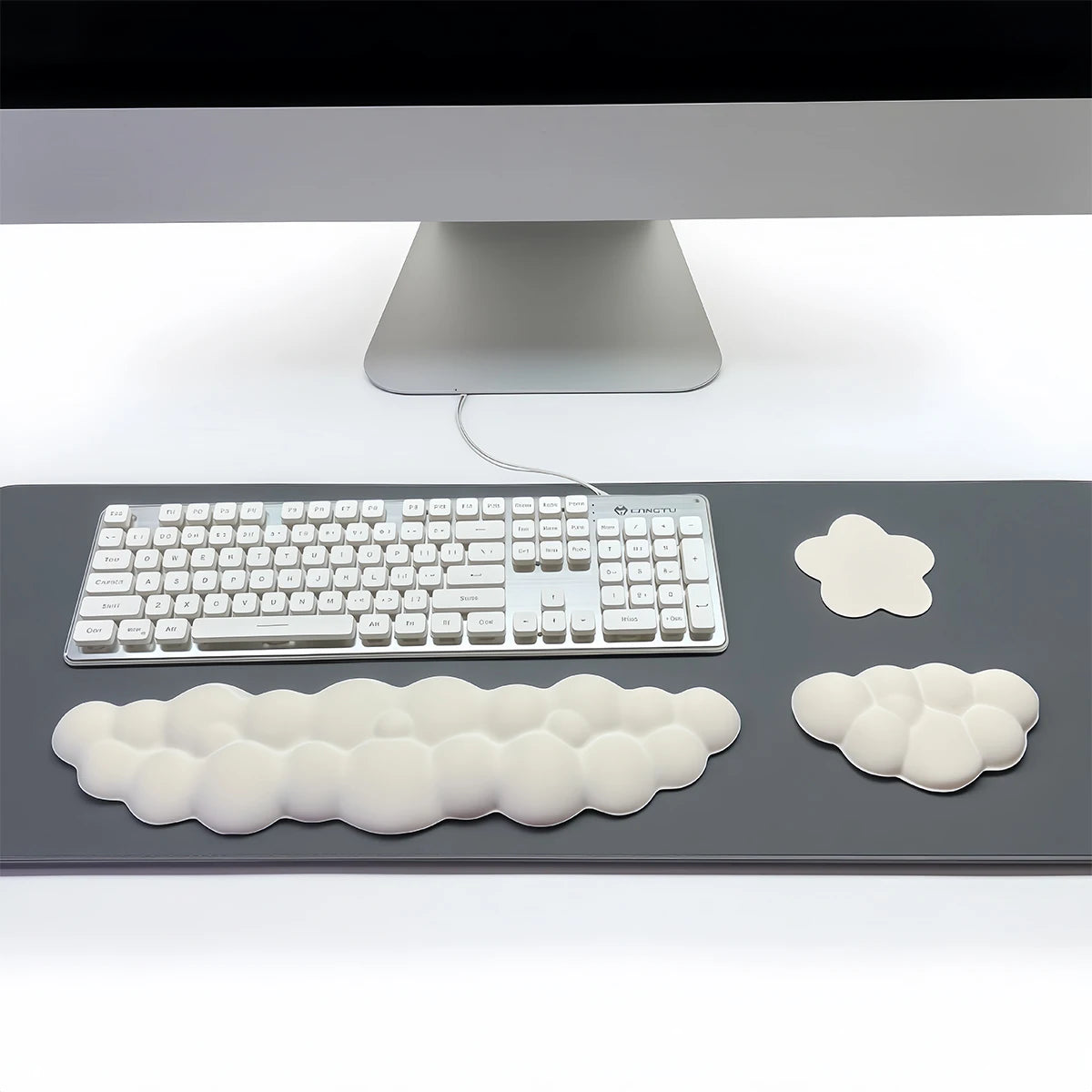 Un set de trois repose-poignets en forme de nuage blanc et un clavier argenté sur une surface gris foncé.