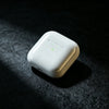 A white True Wireless Earbuds with an indicator light resting on a dark, textured surface.