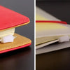 A close-up view of a red and yellow binder pocket with a white zipper, designed for notebooks.