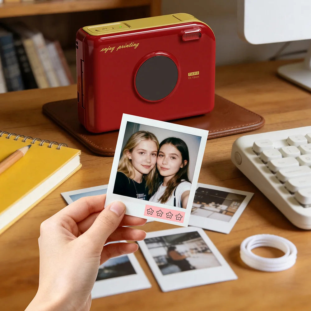 A hand holds a red smart Bluetooth label maker device next to various photo prints and paper on a wooden table.