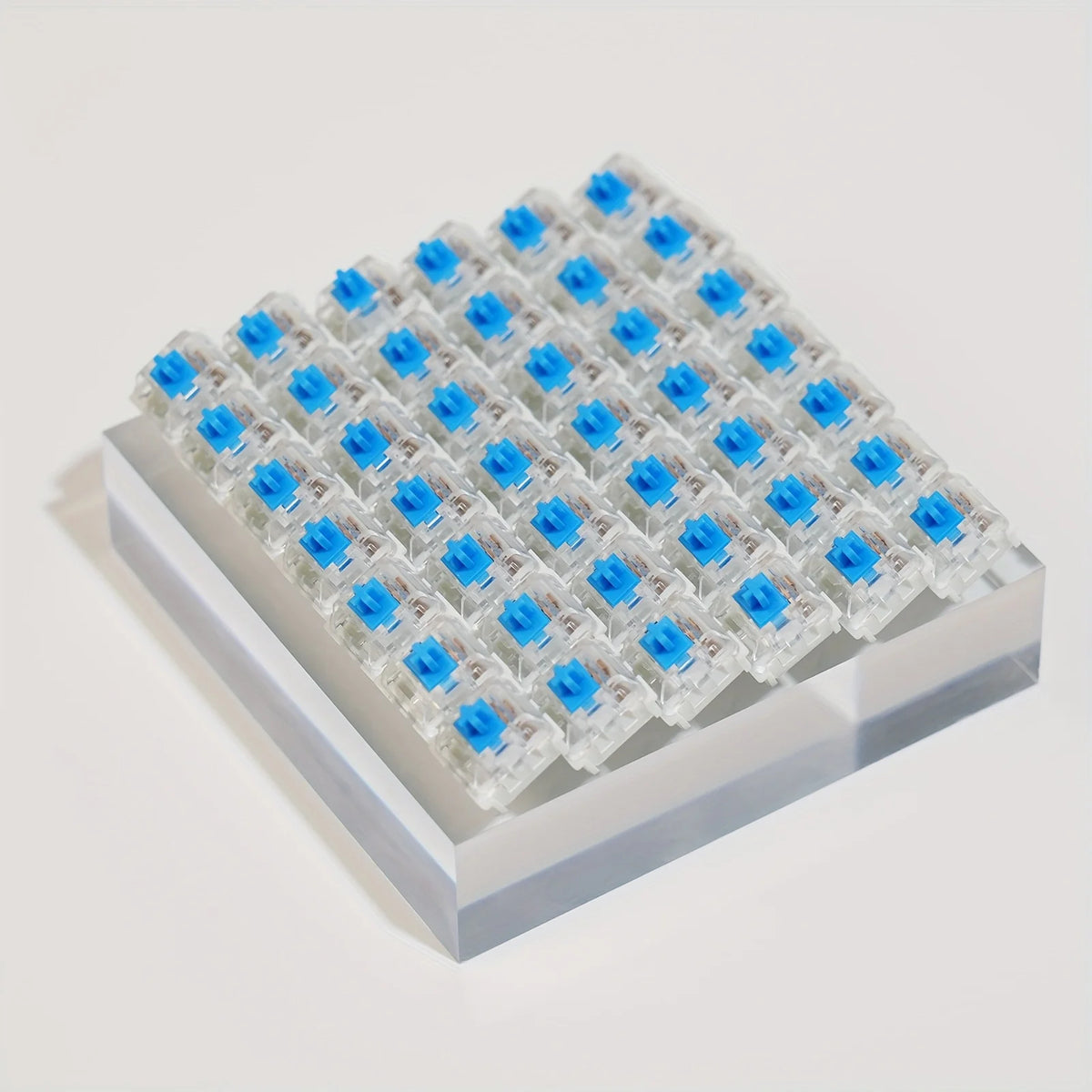 A grid of small plastic keyboard switches with blue accents and a keycap puller set displayed on a white surface.